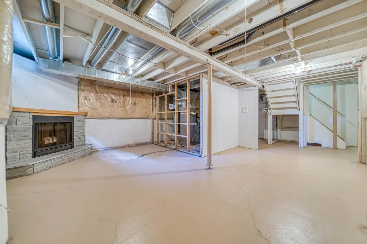 The basement before: bare joists, a stone fireplace and a concrete floor.