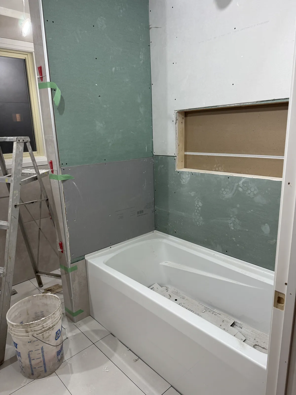 The bathroom mid-renovation: a new tub set against waterproof board, with a framed niche.