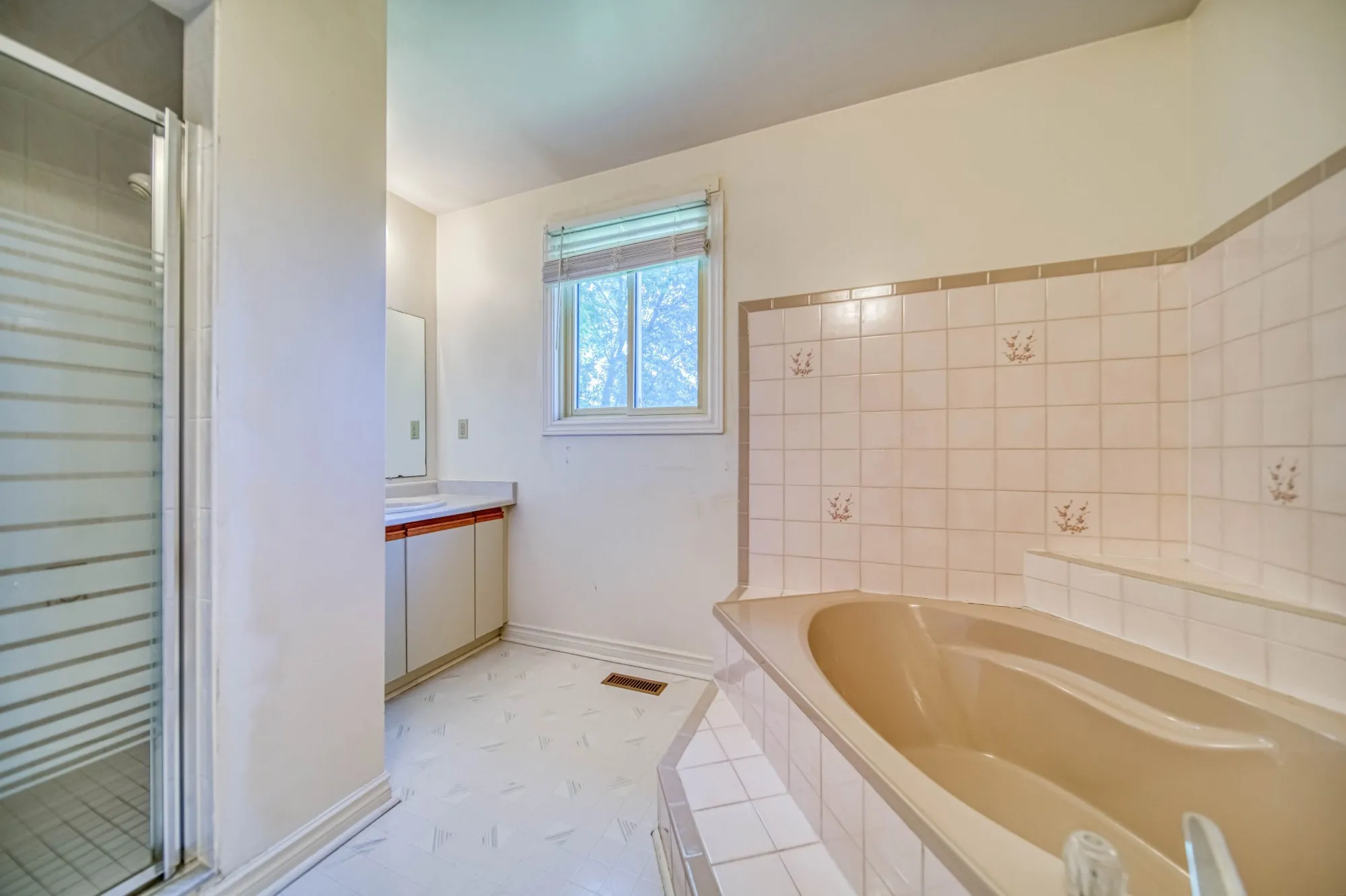 The ensuite before: a beige corner tub, a small vanity and a framed shower.