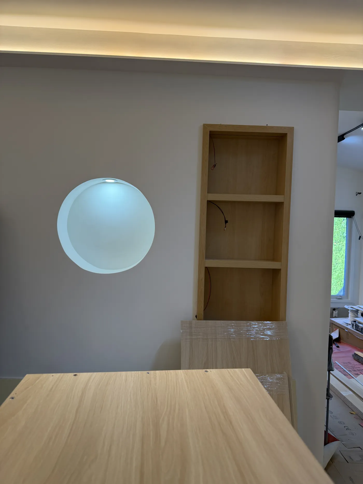The same wall on site: the round niche and oak shelf built and lit.