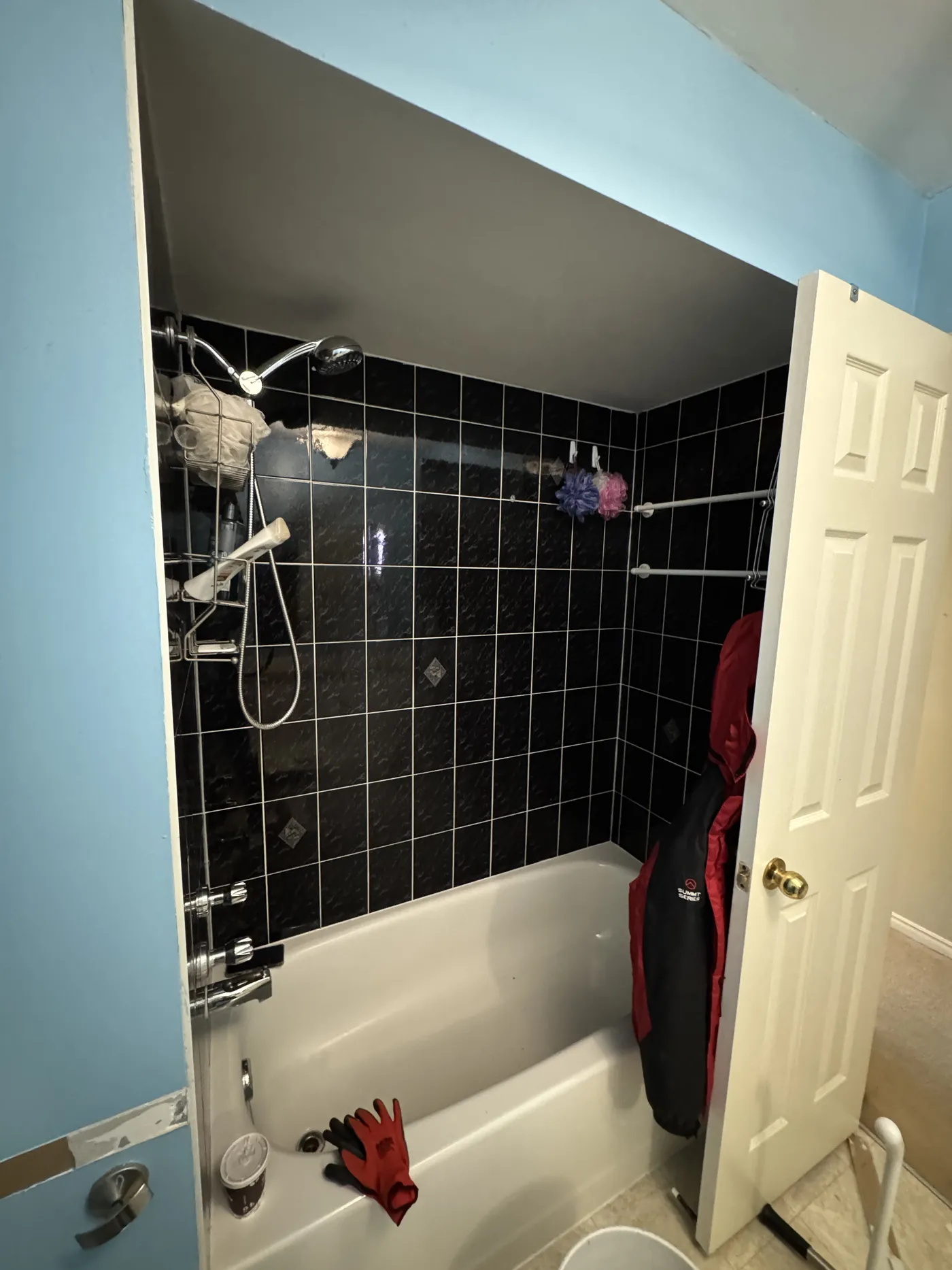 A bathroom before: blue walls and a black tiled tub.