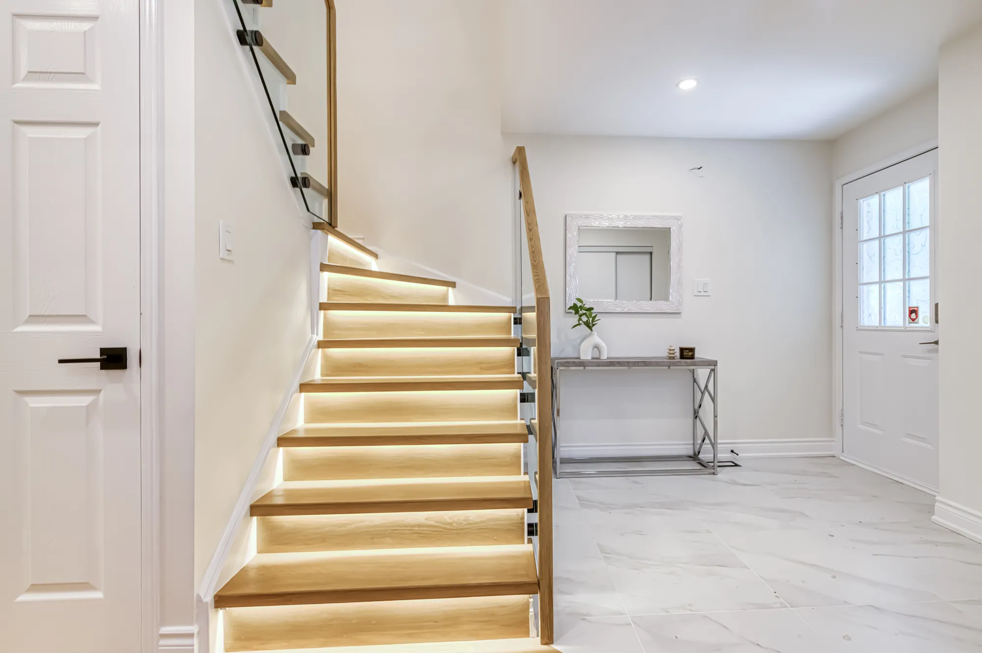 The finished entry: oak treads lit from beneath, behind glass.