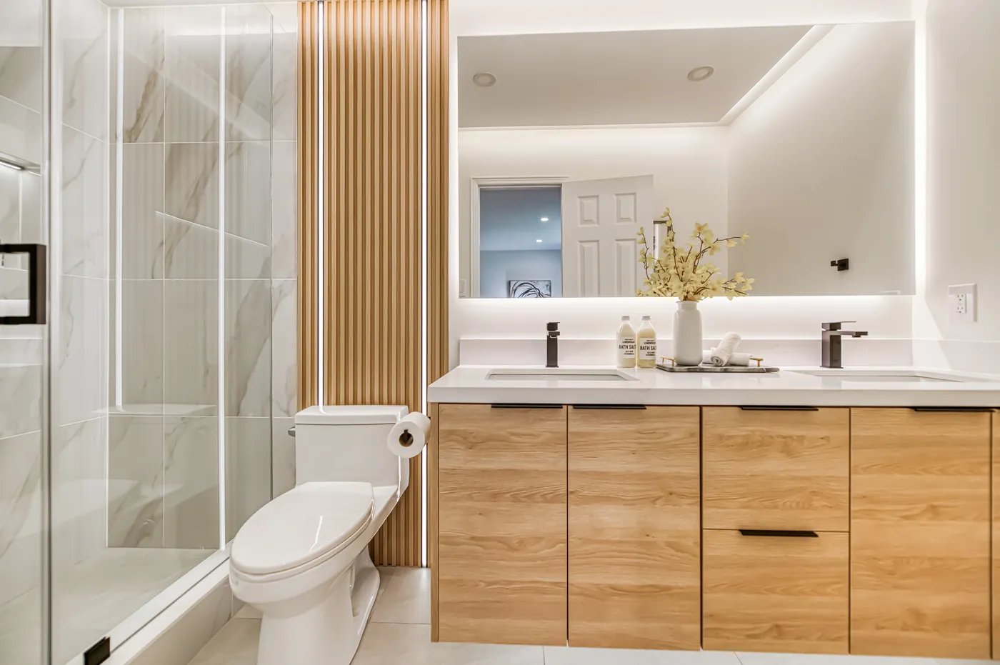 The ensuite: an oak vanity, a lit mirror and a glass shower.