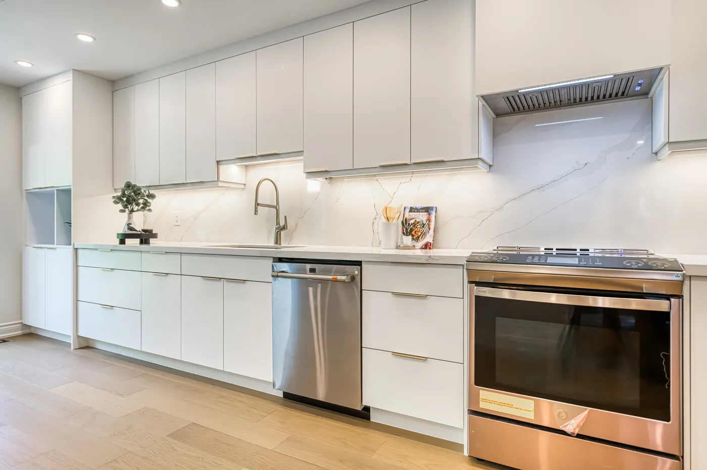The finished kitchen: flat white cabinets along one wall with a marble backsplash.
