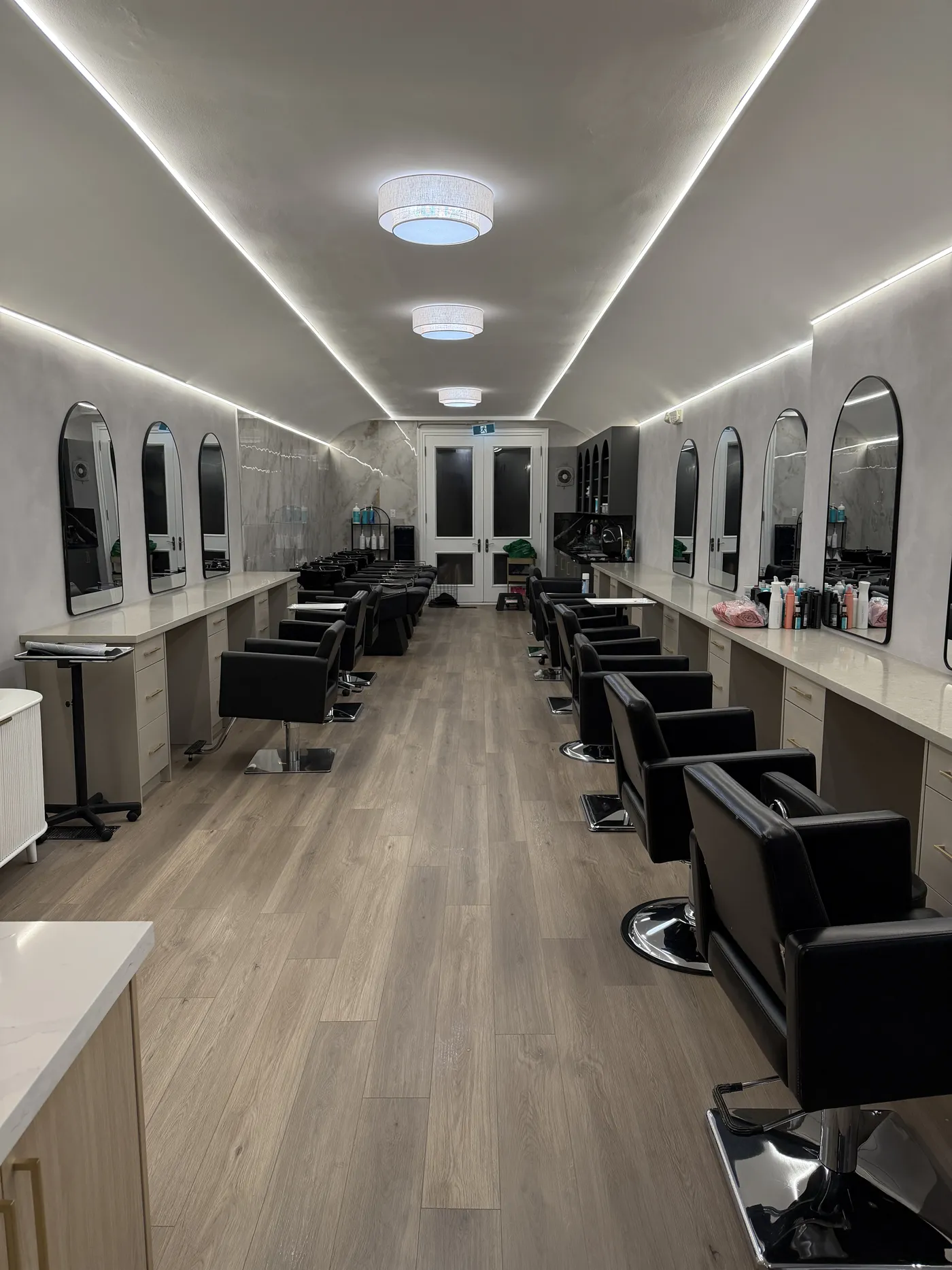 The finished salon: light floors, plaster walls, arched mirrors and lines of light in the ceiling.
