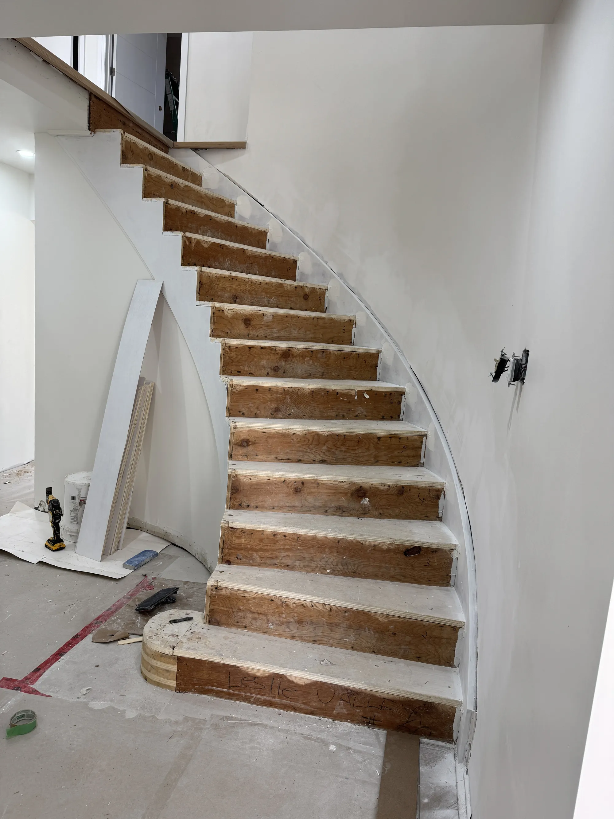 The same staircase mid-renovation: carpet stripped to raw wooden treads, new drywall on the curve.